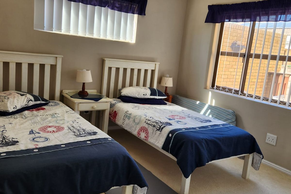 A functional bedroom featuring neutral wall tones, carpeted flooring, and dual windows fitted with vertical blinds.