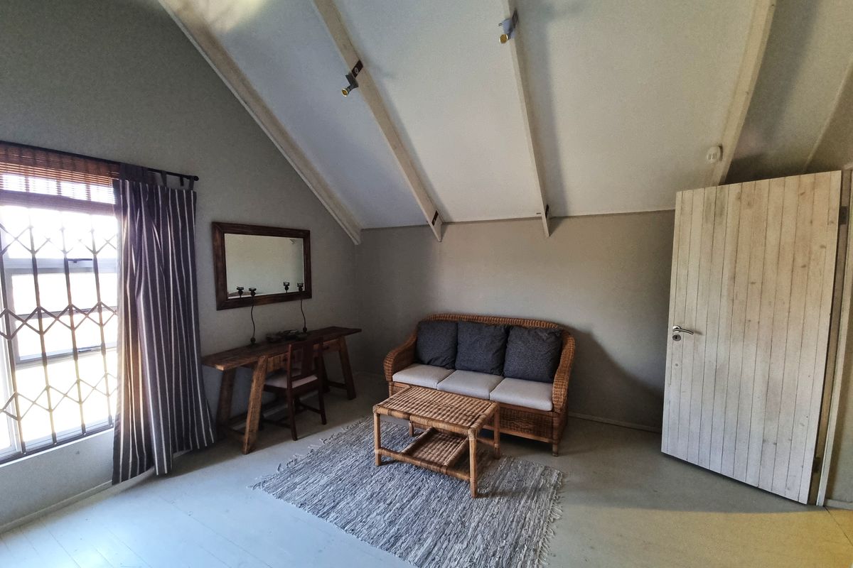 A living room featuring a high vaulted ceiling with exposed rafters, neutral wall finishes, and a window fitted with a security gate.