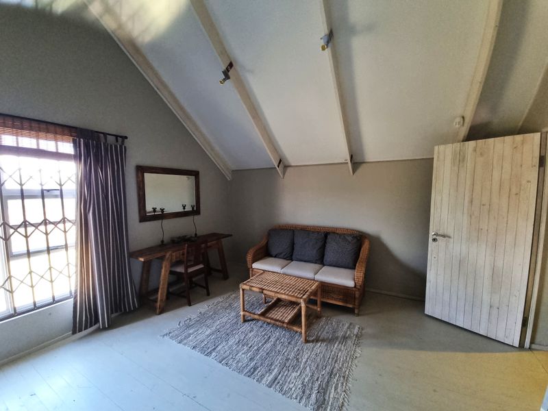 A living room featuring a high vaulted ceiling with exposed rafters, neutral wall finishes, and a window fitted with a security gate.