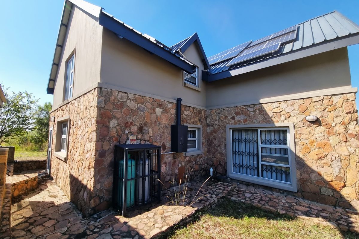 Rear elevation of a house featuring stone cladding, a metal roof with solar panels, and secure window gates.