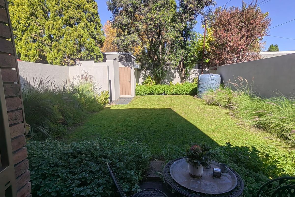 A well-maintained private rear garden featuring a lush lawn, perimeter boundary walls, a storage shed, and a water tank.