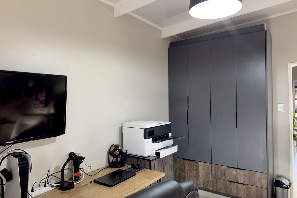A functional home office or bedroom featuring a large, modern built-in wardrobe with a two-tone grey and wood-grain finish.