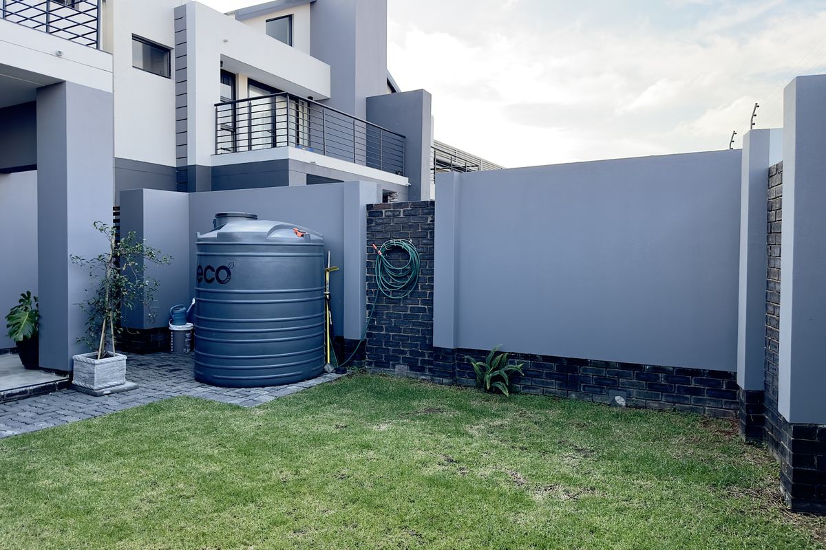 A private rear garden area featuring a paved section, a large water storage tank, and a modern boundary wall with brick detailing.