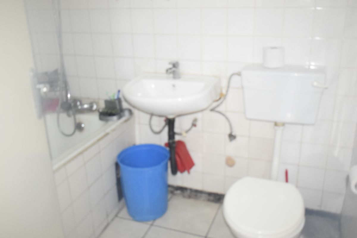 A functional bathroom featuring a wall-mounted basin, toilet, and bathtub with tiled wall finishes, currently showing signs of wear and exposed plumbing.