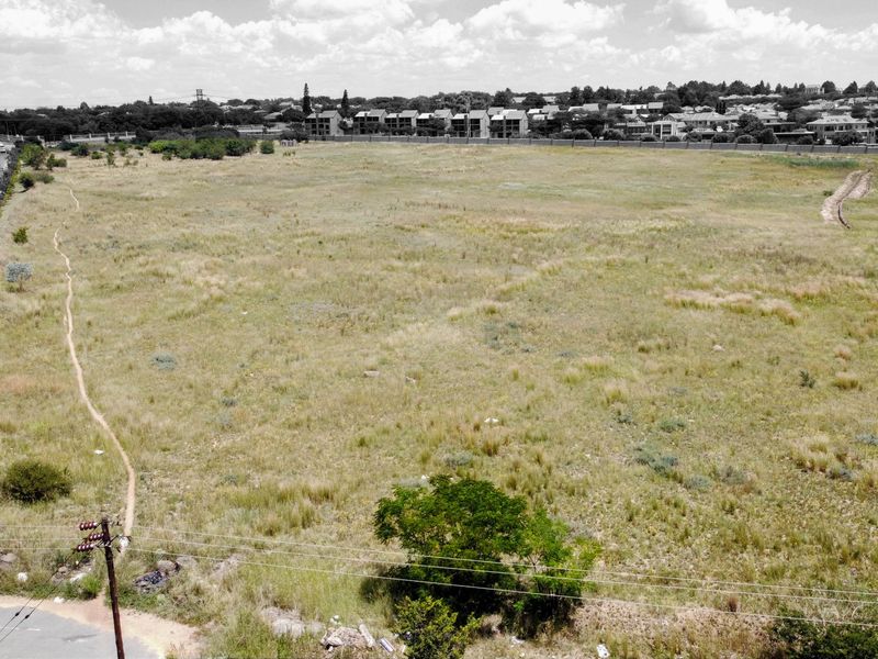 An aerial view of a large, vacant residential plot of land situated near a road and established residential neighborhood.