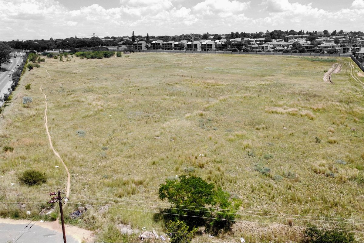 An aerial view of a large, vacant residential plot of land situated near a road and established residential neighborhood.