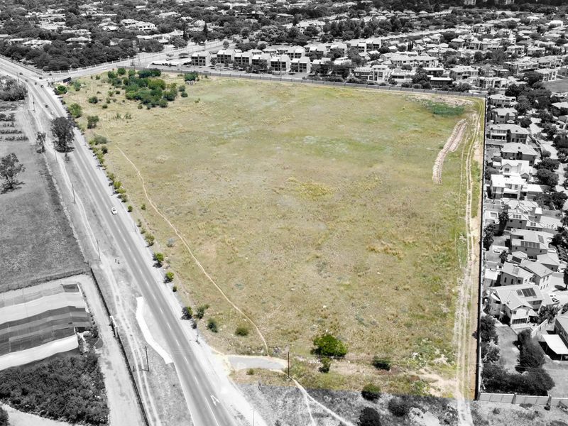 An aerial view of a large, vacant residential land parcel situated adjacent to an established suburban neighborhood and a main access road.