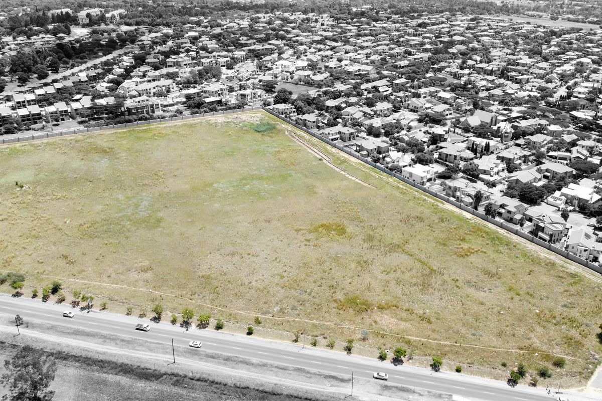 An aerial view of a large, vacant residential plot situated in a developed suburban neighborhood, adjacent to a main road.