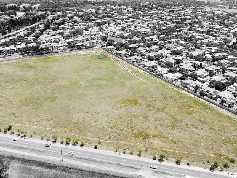 An aerial view of a large, vacant residential plot situated in a developed suburban neighborhood, adjacent to a main road.