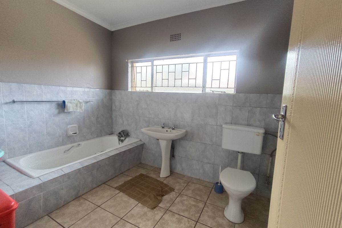 A functional bathroom featuring a pedestal basin, built-in bathtub, and toilet, finished with neutral wall and floor tiling.
