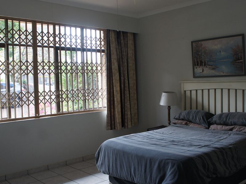 A bedroom featuring tiled flooring, a ceiling fan, and a window fitted with a metal security gate.