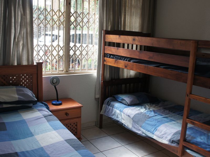A bedroom featuring tiled flooring and a window fitted with a security gate.