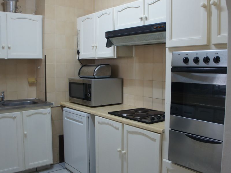 A functional kitchen featuring white cabinetry, a double sink, built-in oven, electric hob, and extractor fan with tiled backsplash.
