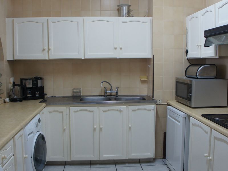 A functional kitchen featuring white cabinetry, a double sink, integrated hob, and extractor fan, with tiled backsplash and flooring throughout.