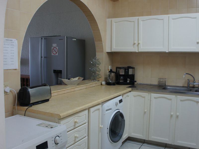 A functional kitchen featuring white cabinetry, laminate countertops, a stainless steel sink, and a tiled backsplash, framed by a decorative archway.