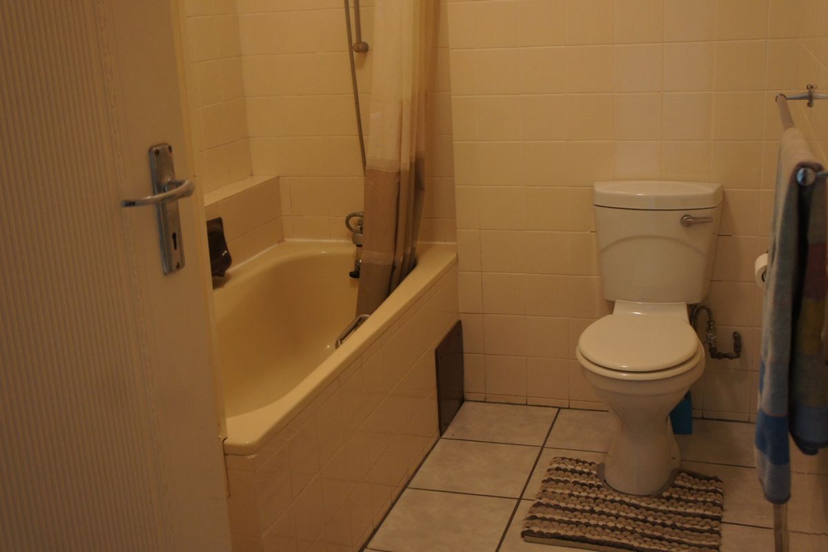 A functional bathroom featuring a built-in bathtub with shower mixer, a standard toilet, and tiled wall and floor finishes.