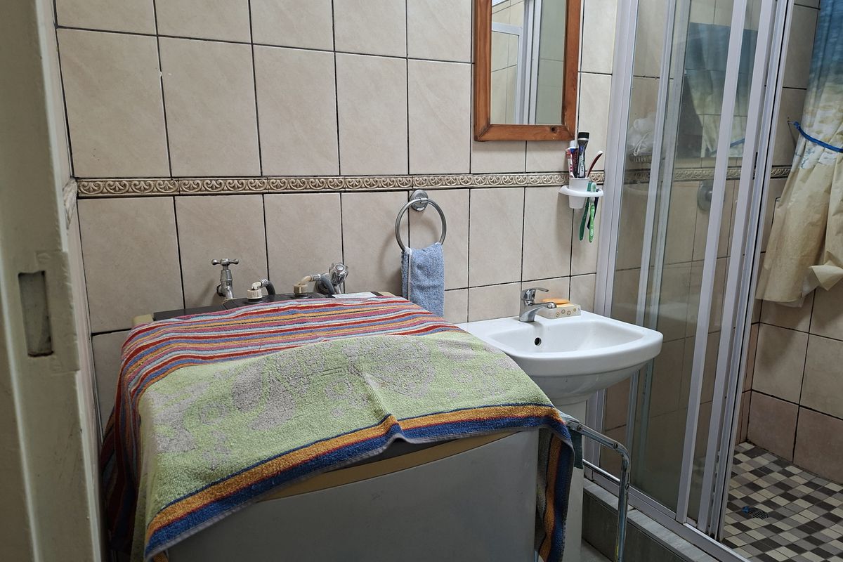 A functional bathroom featuring a pedestal basin, a shower enclosure with a glass door, and tiled walls with a decorative border.