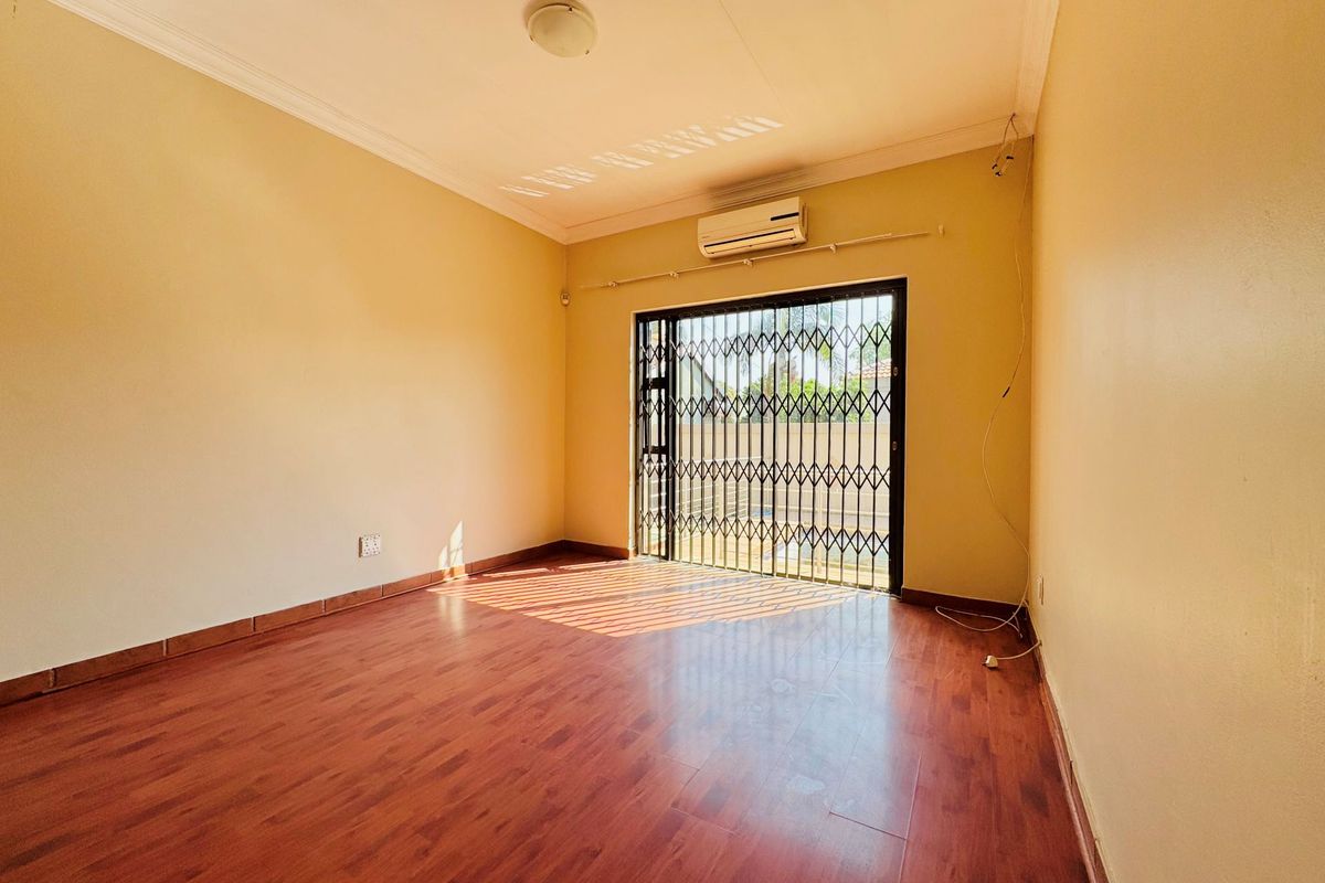 An empty bedroom featuring wood-look laminate flooring, a wall-mounted air conditioning unit, and a secure metal sliding gate leading to the exterior.