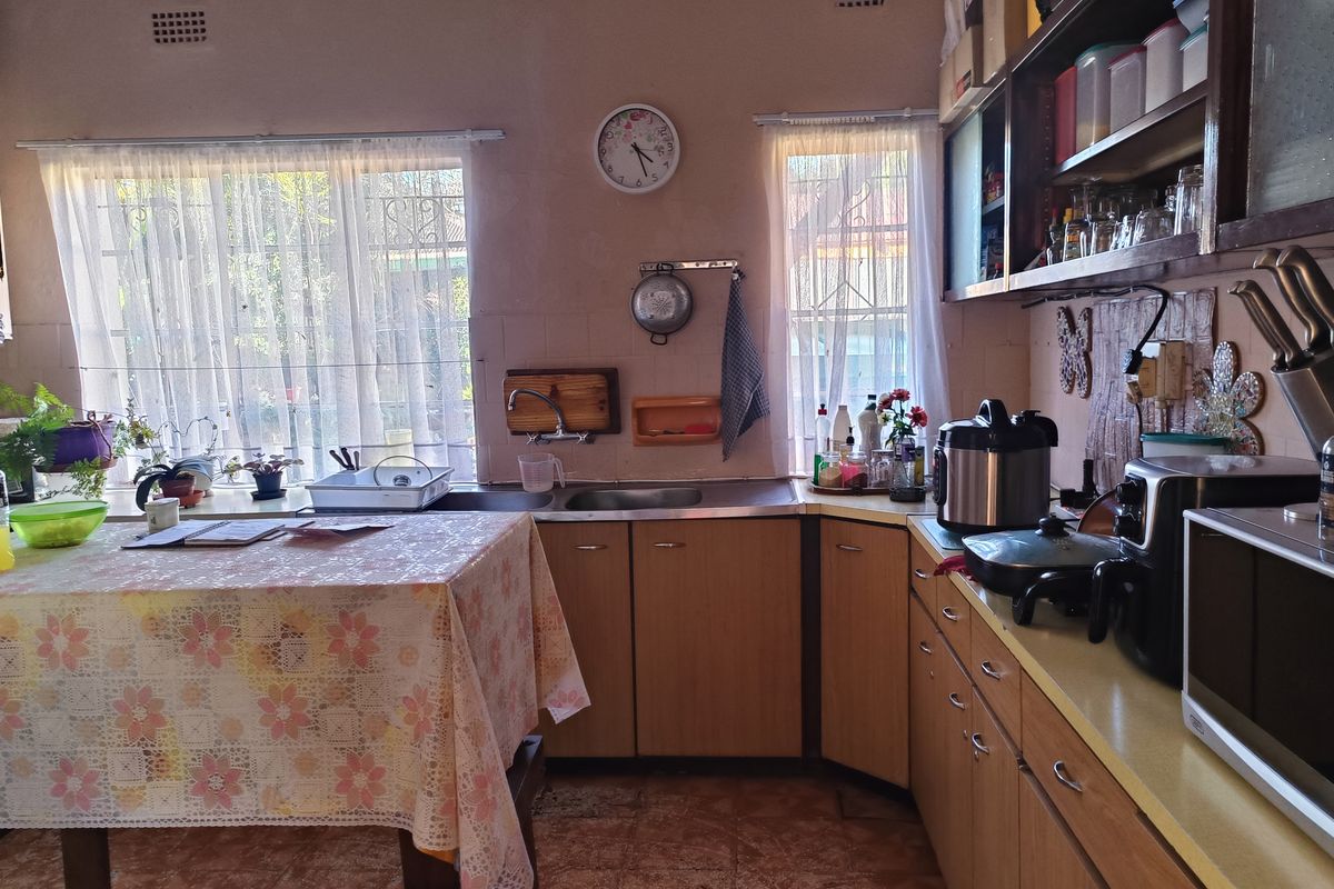 A dated kitchen featuring laminate cabinetry, laminate countertops, and a stainless steel sink, with security bars installed on the windows.