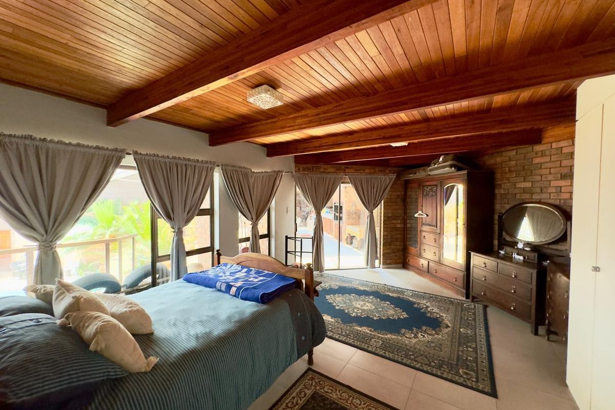 Spacious bedroom featuring a warm timber-beamed ceiling, exposed brick accent wall, tiled floors, and sliding glass doors providing access to the outdoor area.