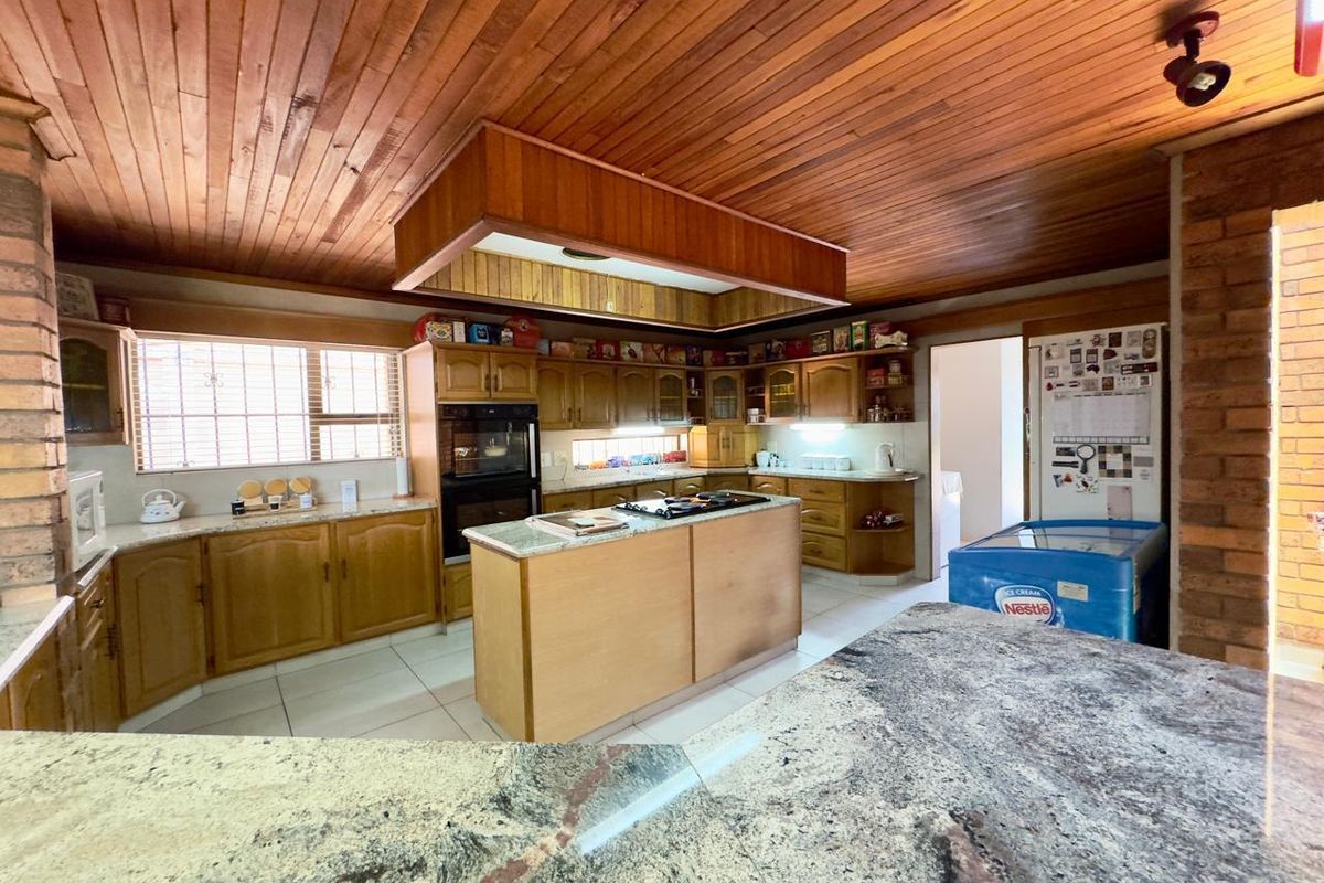 Spacious kitchen featuring timber ceilings, exposed brick accents, granite countertops, and a central island with a built-in hob and oven.