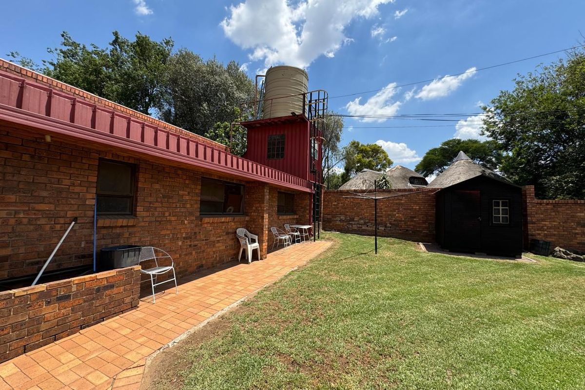Rear exterior view featuring a brick house facade, paved patio area, elevated water tank, and a garden shed set within a lawned backyard.