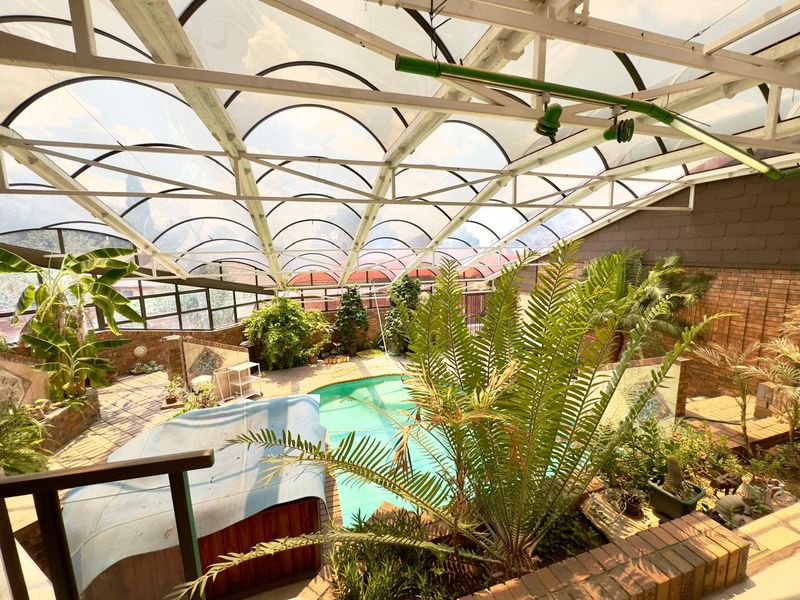 Enclosed indoor pool area featuring a large curved polycarbonate roof structure, brick wall finishes, and integrated planter boxes surrounding the swimming pool.