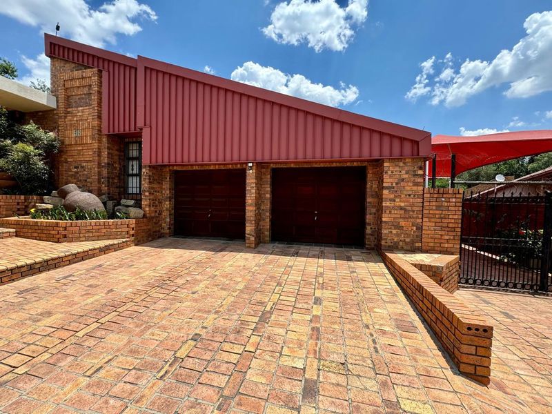 Front exterior view of a house featuring a double garage, brick facade, and a paved driveway with retaining walls.