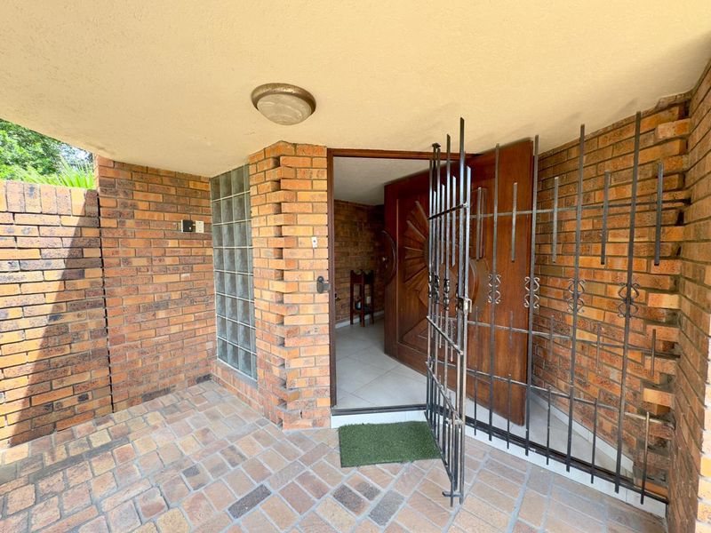 Covered entrance area featuring a solid wood front door, security gate, brick facade, and glass block detailing.