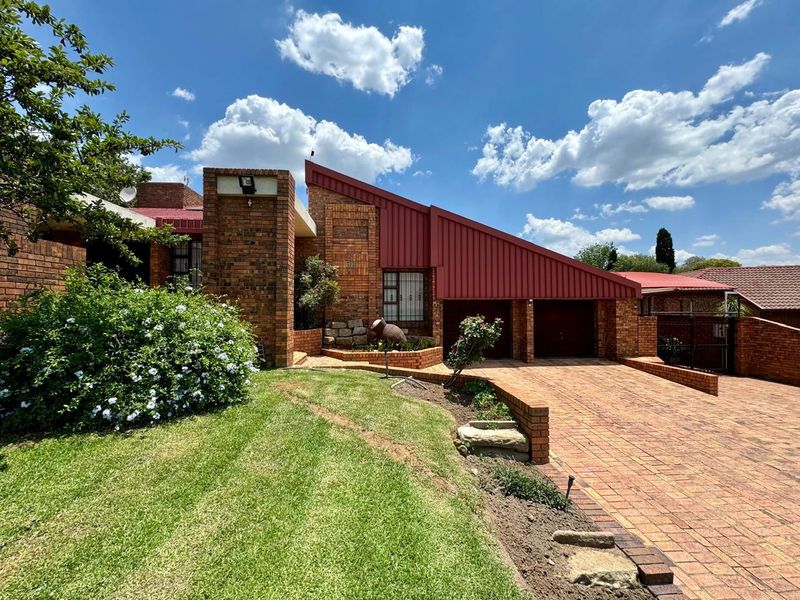 Front elevation of a face brick house featuring a distinctive sloped metal roof, paved driveway, and double garage access.
