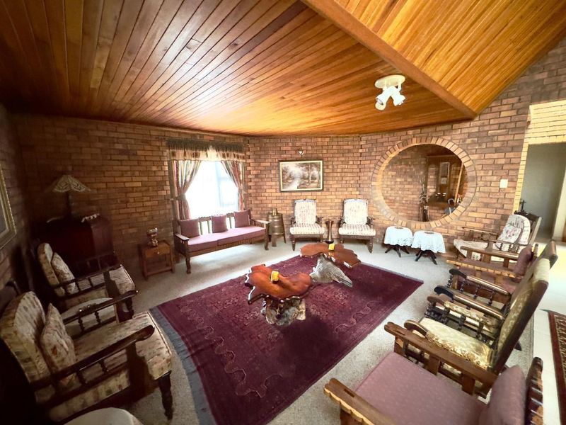 Spacious living room featuring exposed brick walls, a high timber-clad ceiling, and a unique circular feature window, offering a warm and rustic aesthetic.