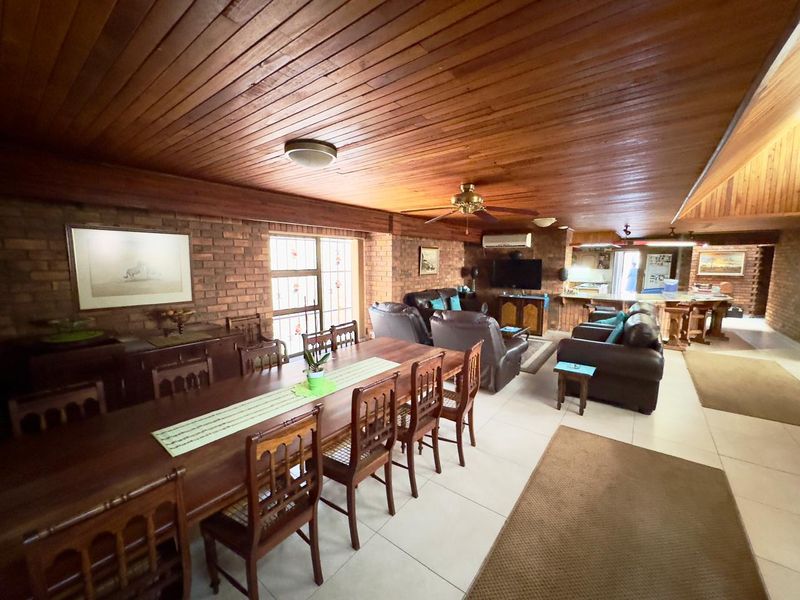 Spacious open-plan living and dining area featuring exposed brick walls, a warm timber ceiling, and tiled flooring, creating a rustic and inviting atmosphere.
