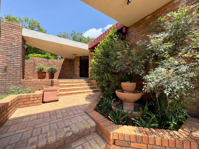 A well-maintained brick entrance area featuring tiered brick paving, retaining walls, and a concrete architectural overhang leading to the front door.