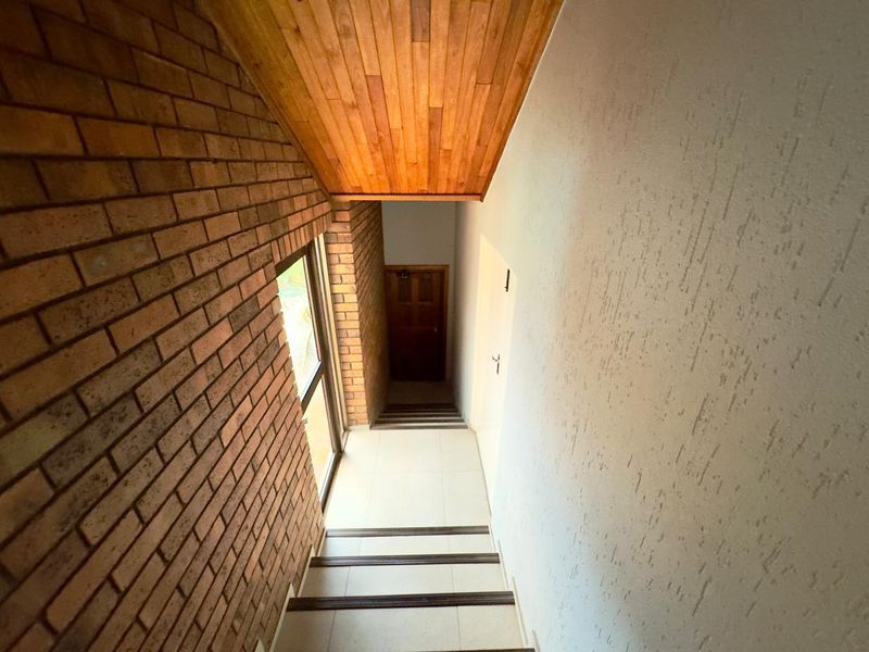A staircase hallway featuring exposed brickwork, a timber-clad ceiling, and tiled steps with safety nosing.