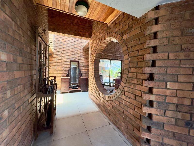 A unique entrance hall featuring exposed brickwork, a distinctive circular feature window, timber ceiling accents, and neutral tiled flooring.