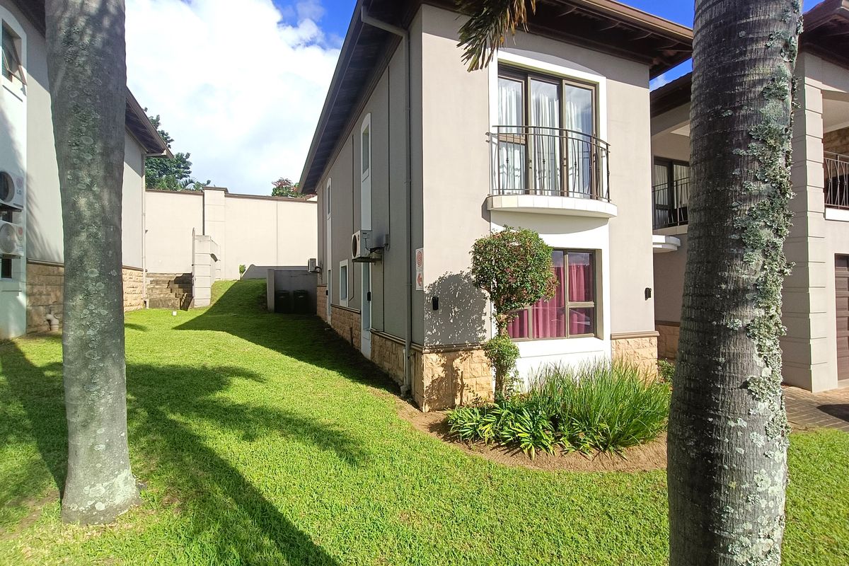 Rear view of a townhouse featuring stone cladding, a small balcony with wrought iron railing, and a well-maintained lawn area.
