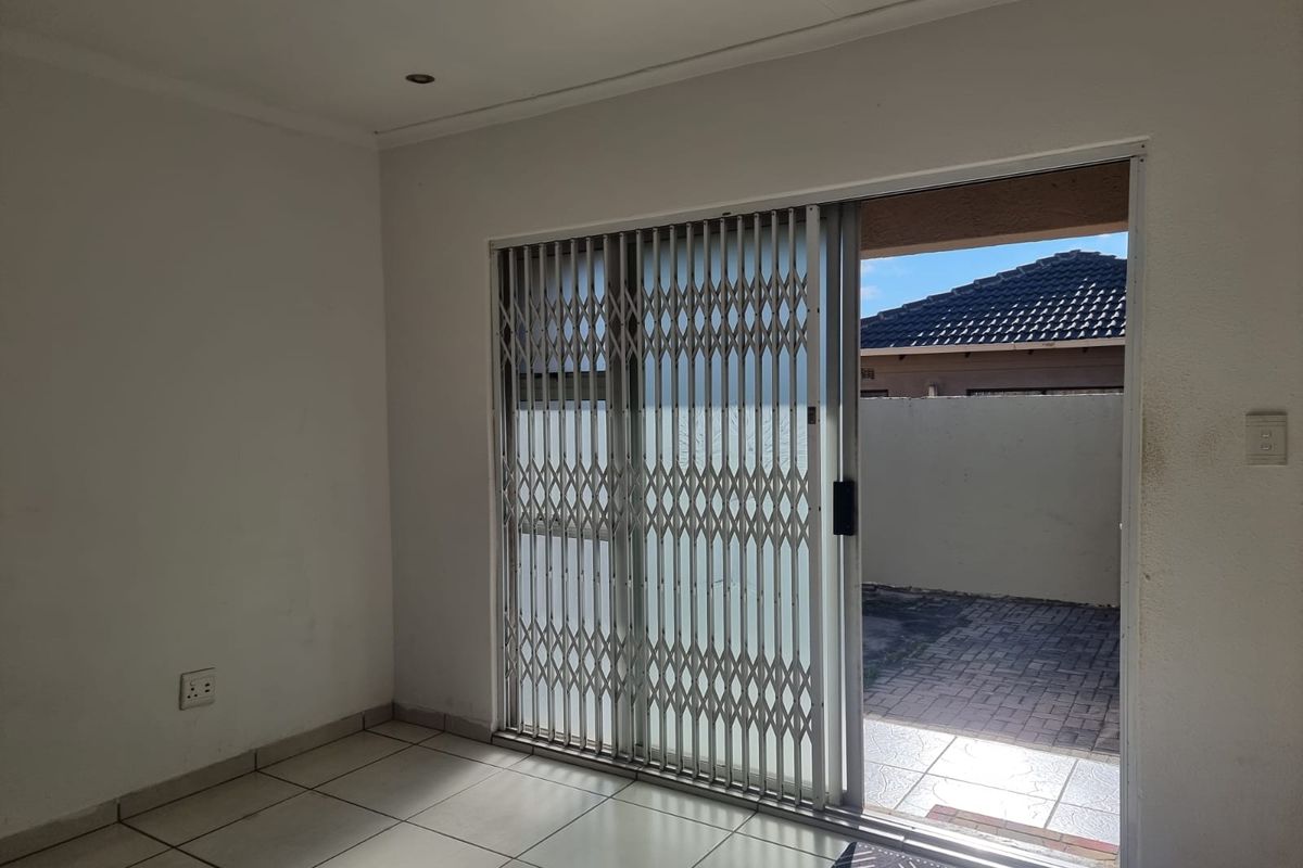 Interior living space featuring tiled flooring and a sliding glass door with a security gate leading to an outdoor patio area.