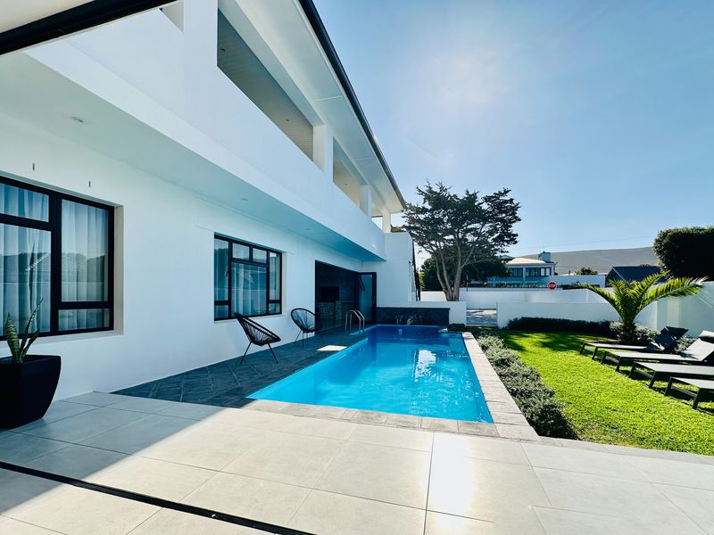 Modern outdoor living area featuring a sleek swimming pool, tiled patio space, and a well-maintained lawn, perfect for relaxation and entertaining.