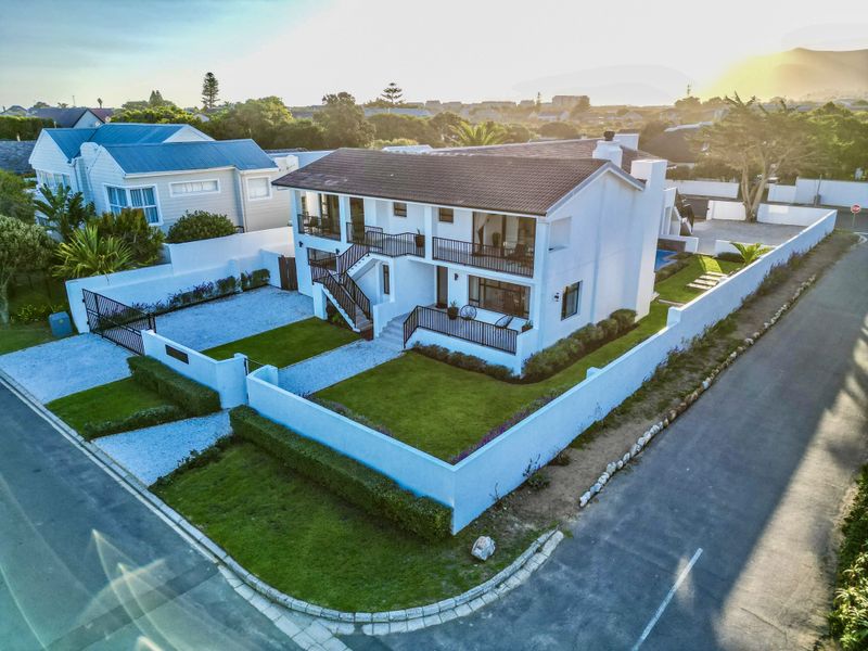 Aerial view of a two-story residential property featuring a tiled roof, balconies, landscaped lawn, and secure boundary walls.