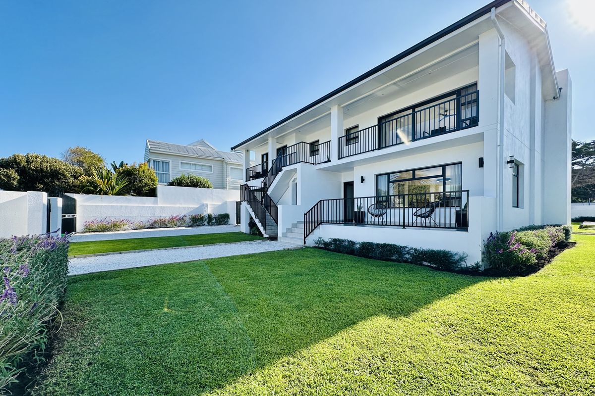 A well-maintained two-story residential exterior featuring a landscaped lawn, gravel driveway, and a spacious balcony with black railings.