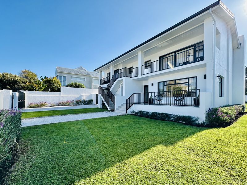 A well-maintained two-story residential exterior featuring a landscaped lawn, gravel driveway, and a spacious balcony with black railings.