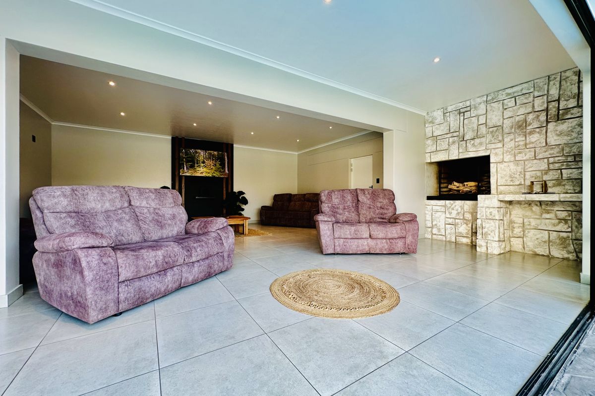 Spacious living area featuring large format floor tiles, recessed downlighting, and a prominent stone-clad fireplace, offering a bright and open atmosphere.