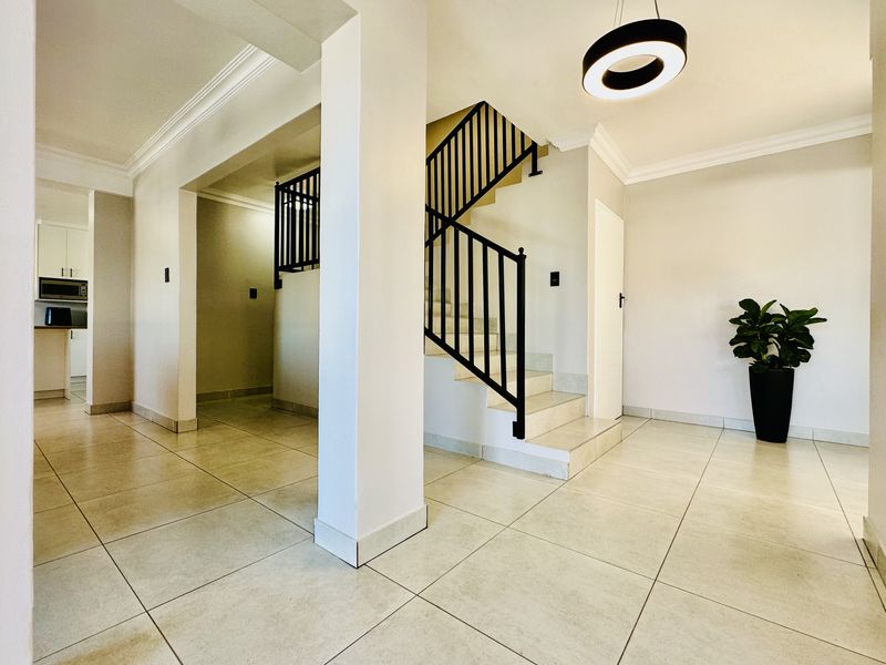 Spacious entrance hall featuring modern tiled flooring, a central staircase with a black metal balustrade, and contemporary pendant lighting.