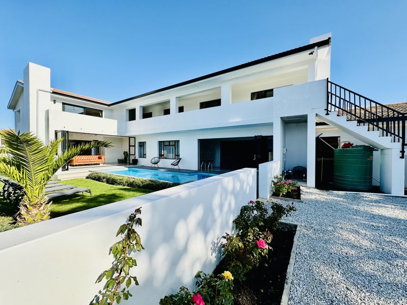 Rear view of a modern two-story house featuring a swimming pool, covered patio area, external staircase, and a well-maintained garden with boundary walls.