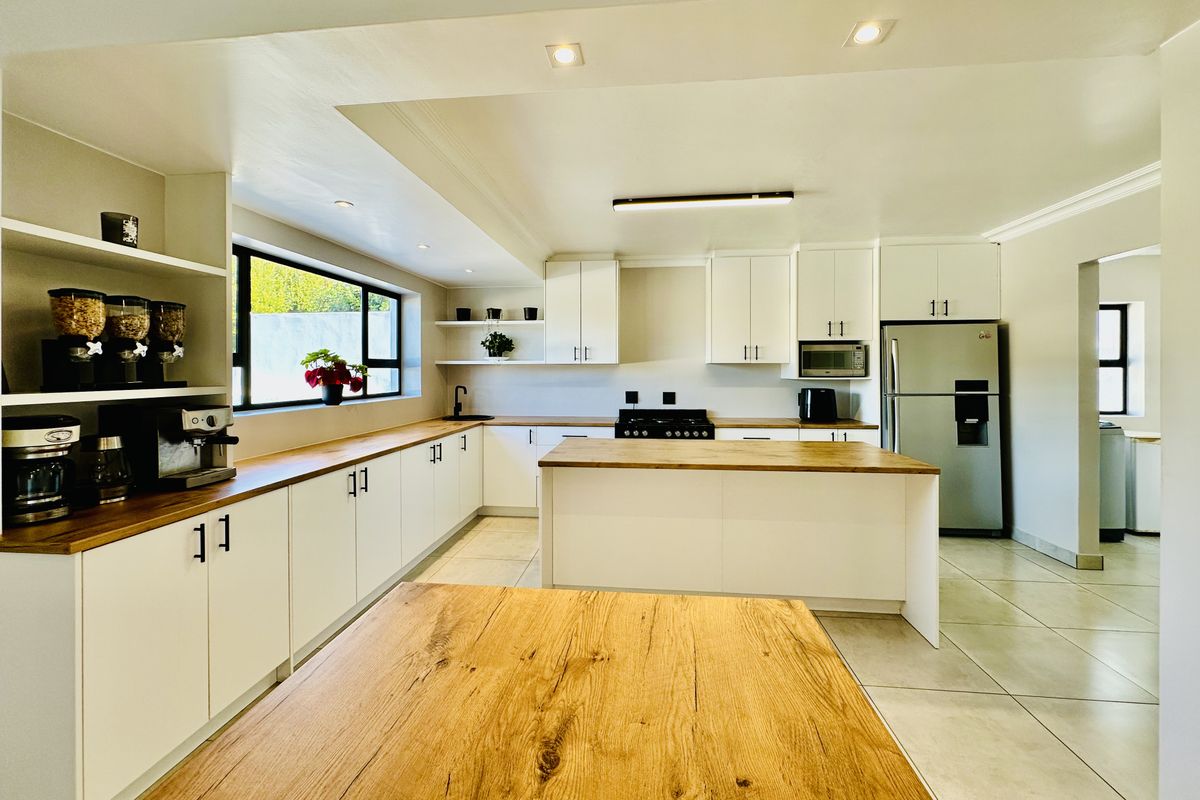 Modern kitchen featuring white cabinetry, wooden countertops, a central island, gas stove, and tiled flooring with ample natural light.