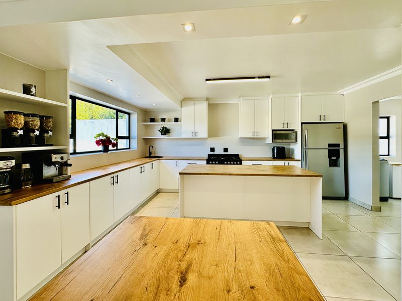 Modern kitchen featuring white cabinetry, wooden countertops, a central island, gas stove, and tiled flooring with ample natural light.