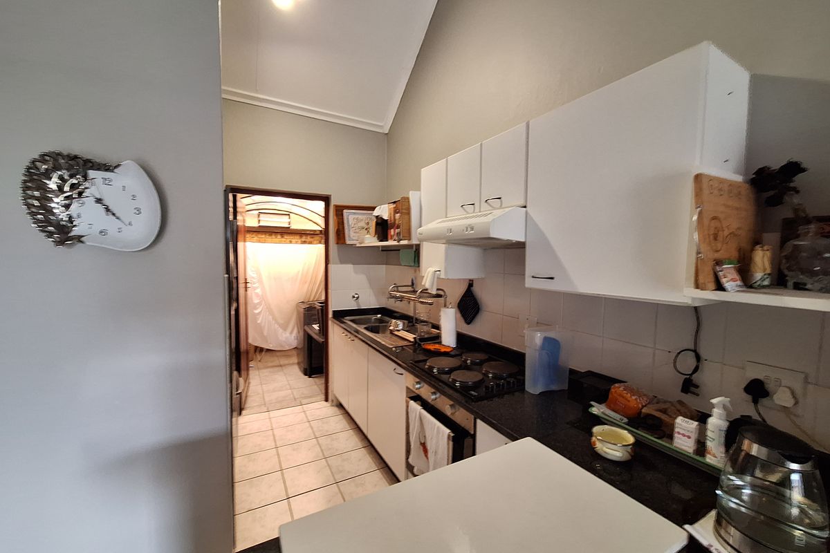 Compact kitchen featuring built-in cabinetry, integrated electric hob, oven, and extractor fan, with tiled flooring and direct access to an adjacent utility area.