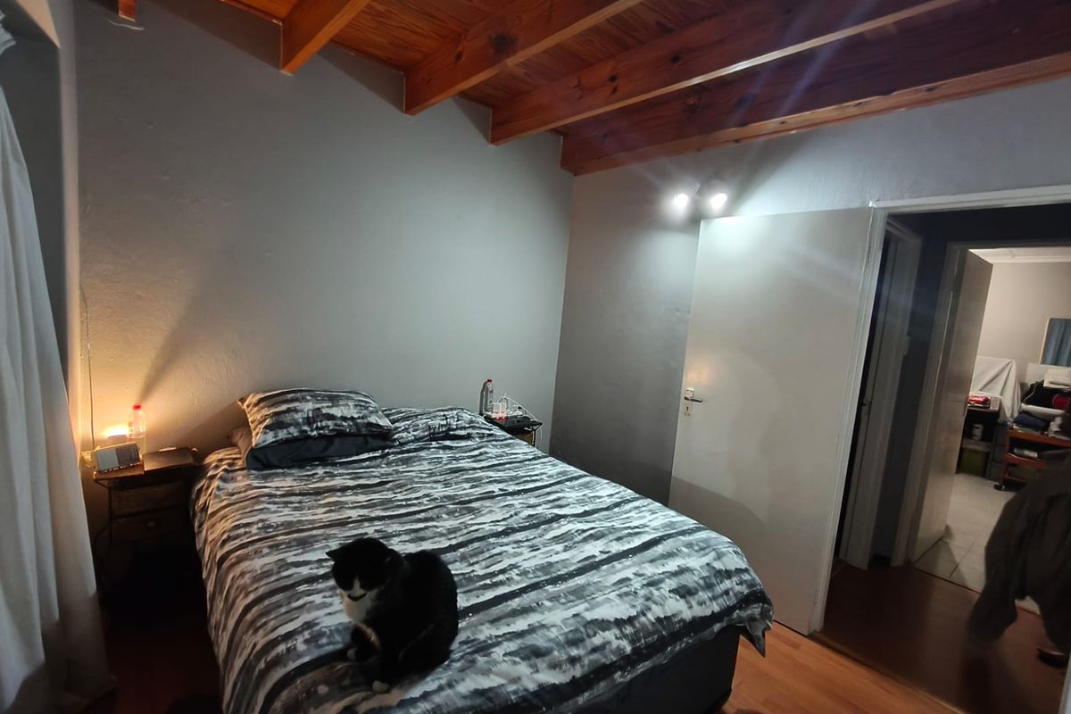 A bedroom featuring exposed timber ceiling beams, laminate flooring, and a doorway leading to an adjacent room.