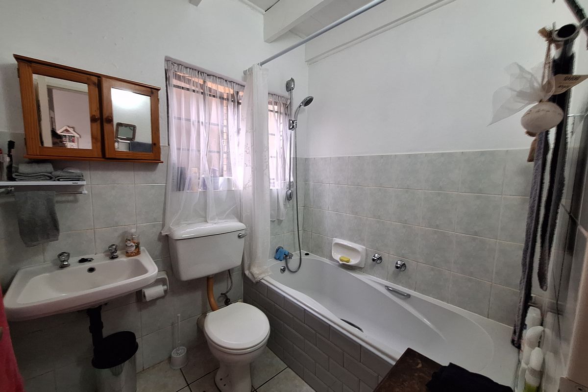 A functional bathroom featuring a bathtub with shower attachment, pedestal basin, and tiled walls, offering a practical layout for a townhouse.