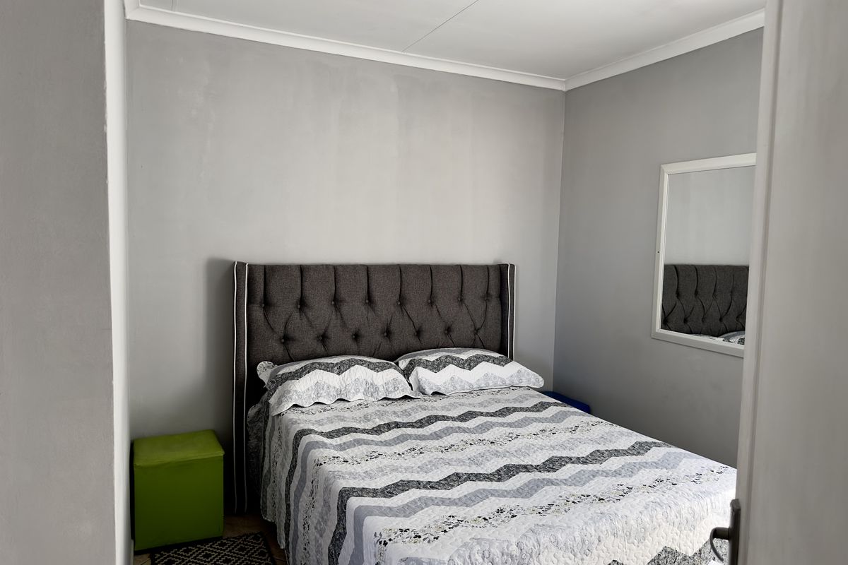 A compact bedroom featuring neutral grey walls, tiled flooring, and a built-in mirror, offering a functional and clean living space.